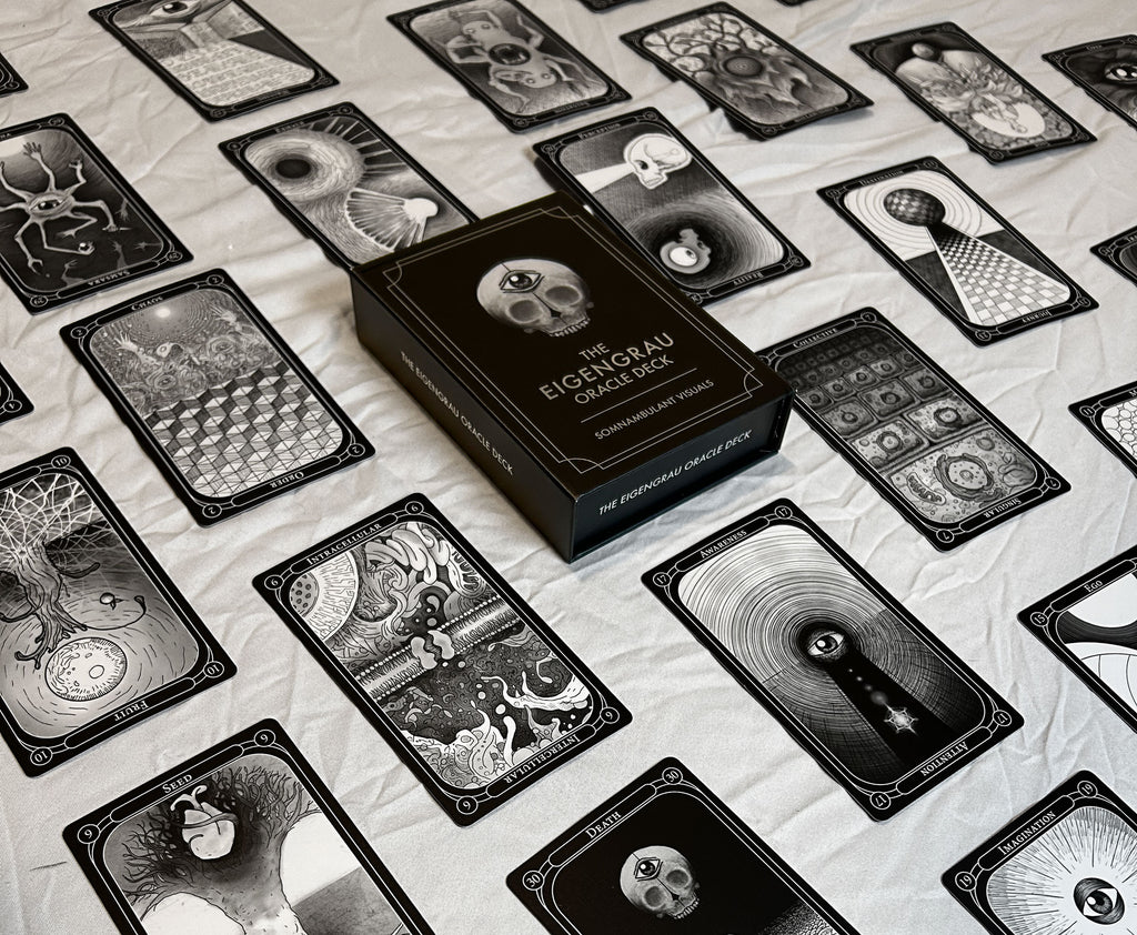A black-and-white box labeled "The Eigengrau Oracle Deck Limited Drop" by Rage Create rests on a cloth, surrounded by hand-drawn oracle cards with abstract and surreal designs.