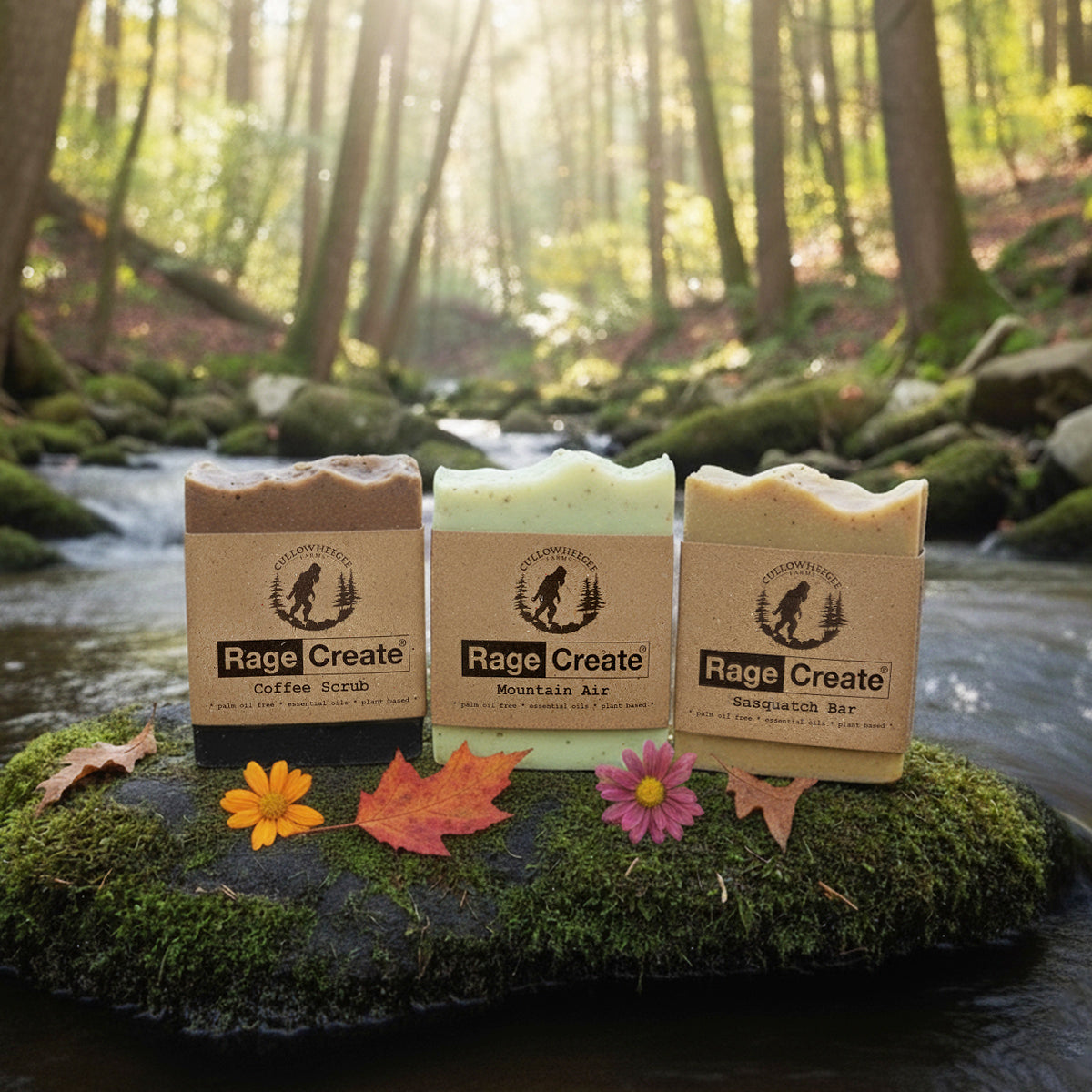 Three limited edition Rage Create Bar Soap 3-Pack bars rest on a mossy rock in a forest stream, surrounded by autumn leaves and flowers. Sunlight highlights their eco-friendly packaging from Rage Create.