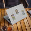 Three vibrant tarot-inspired sticker designs featuring psychedelic animals and mystical symbols applied to a silver laptop, displayed on a wooden outdoor table with beverages nearby.