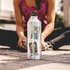 White aluminum water bottle featuring vibrant oracle card stickers with tiger and jellyfish designs, held by a person in a magenta tank top outdoors on pavement.
