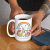 Person with a geometric tattoo holding a white ceramic mug featuring a fox, rainbow, mushrooms, and clouds with the text 'Go the F*ck Outside' while seated at a wooden table.