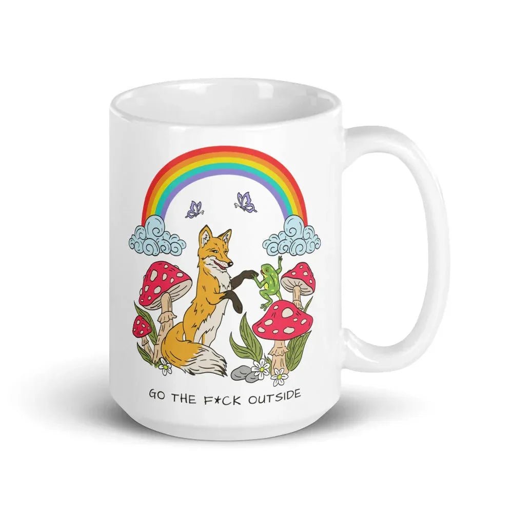 White ceramic mug featuring a whimsical forest scene with a smiling fox, red and white spotted mushrooms, butterflies, clouds, and a bright rainbow overhead with the text 'GO THE F*CK OUTSIDE' at the