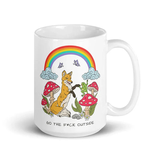 White ceramic mug featuring a whimsical forest scene with a smiling fox, red and white spotted mushrooms, butterflies, clouds, and a bright rainbow overhead with the text 'GO THE F*CK OUTSIDE' at the