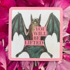 A bat with spread wings holding a pink banner reading 'YOU WILL BE LIFTED' on an illustrated card with a pink border, surrounded by vibrant magenta flowers.