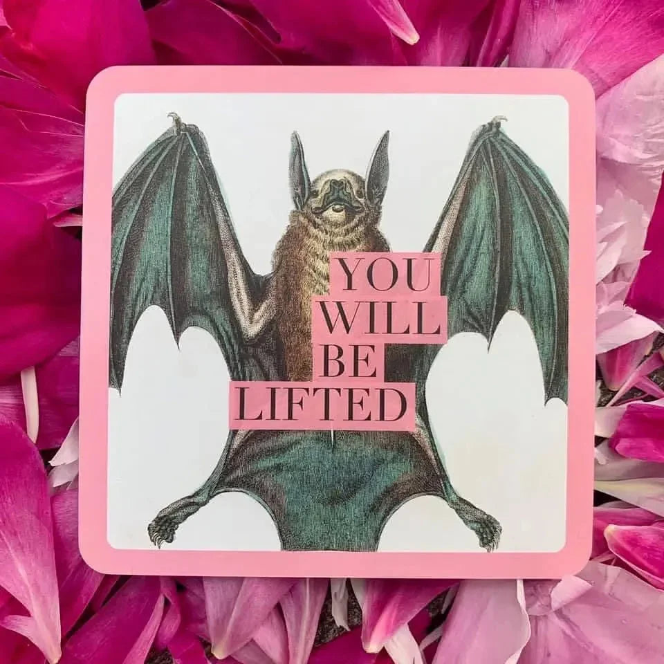 A bat with spread wings holding a pink banner reading 'YOU WILL BE LIFTED' on an illustrated card with a pink border, surrounded by vibrant magenta flowers.