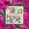 Square cream-colored deck box with "Love Is All We Have" floral design surrounded by vibrant magenta flower petals on dark wood surface.