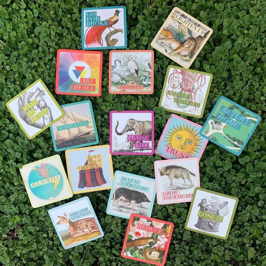 A collection of 60 colorful affirmation cards displayed in a flat lay arrangement on vibrant green moss, featuring illustrated animals, botanical designs, and inspirational text in bold typography on