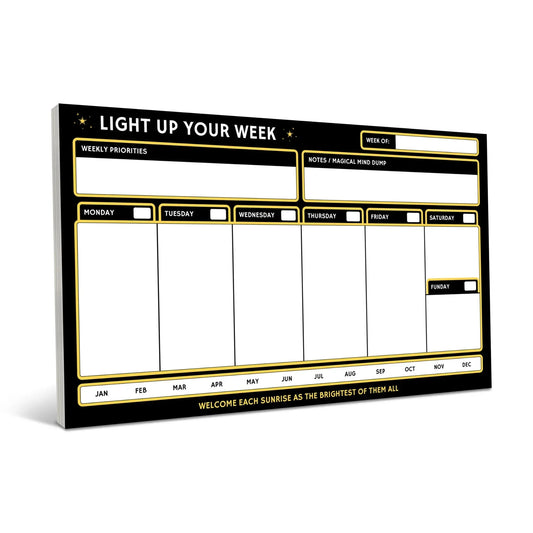 Black weekly planner notepad with gold borders featuring sections for daily schedules Monday through Sunday, weekly priorities, and a notes area, displayed at an angled perspective against a white bac