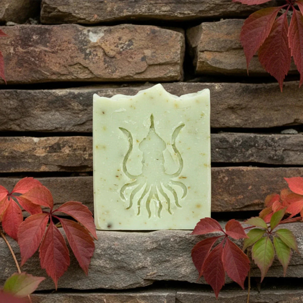 Cream-colored artisan soap bar with carved cthulhu design displayed against weathered brick, surrounded by deep red autumn foliage.