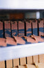 Rows of handmade soap bars stacked vertically, displaying terracotta and blue swirled patterns with dark dividers between each bar in an artisanal arrangement.