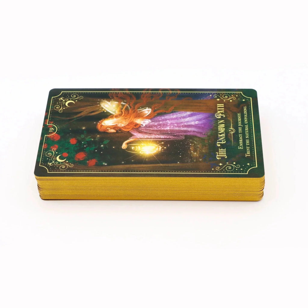Ornate tarot deck box with a mystical fairy figure in a purple gown surrounded by glowing golden lights and red roses on a dark forest background, featuring gold gilded edges and decorative corner flo