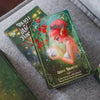 Oracle of the Magical Fairy Forest deck box displaying a luminous fairy with coral-pink hair surrounded by red roses and golden sparkles against a emerald green gradient background.