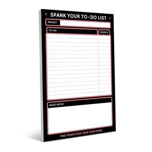 Black notepad with neon pink border featuring "Spank Your To-Do List" header, project field, to-do checklist area, priority box, and magic notes section with motivational tagline at bottom.