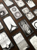 Collection of tarot cards fanned diagonally across dark wood, featuring black-and-white intricate illustrations of eyes, celestial symbols, organic patterns, and mystical imagery with ornate corner de