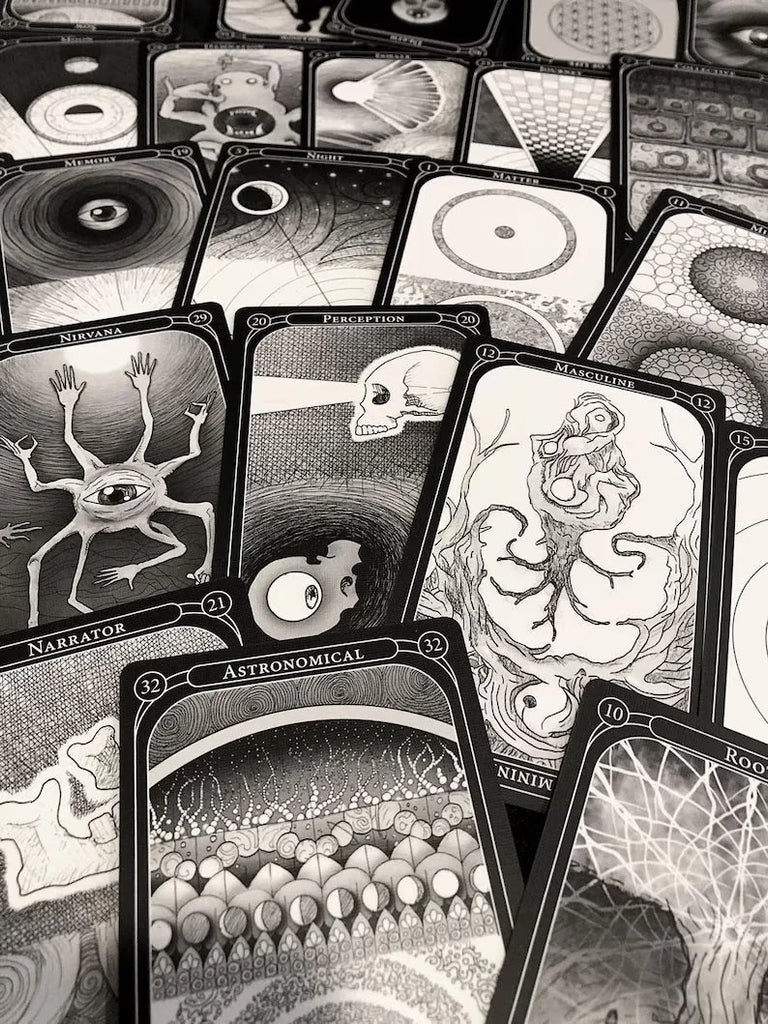 Black and white oracle cards scattered in an overlapping arrangement, featuring surreal detailed illustrations including eyes, hands, skulls, and cosmic patterns on dark borders with numbered labels.