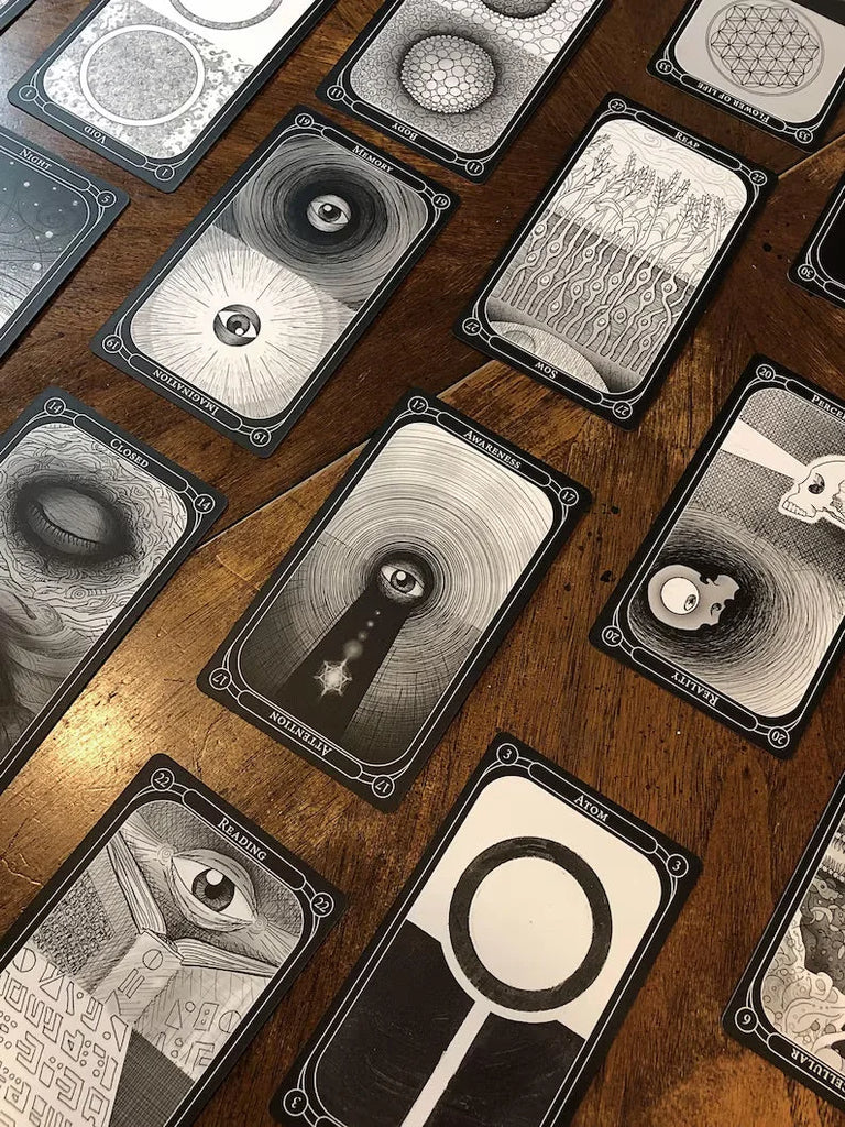 Black and white oracle cards with intricate designs arranged diagonally on a rich wood table, each card featuring geometric patterns, celestial imagery, and hand-drawn illustrations.
